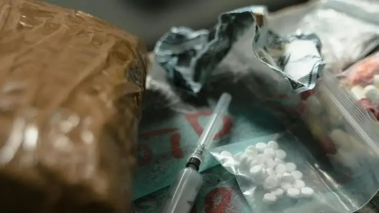 A syringe and small bags containing pills are seen on a table alongside a wrapped package. Credit: MART PRODUCTION / Pexels