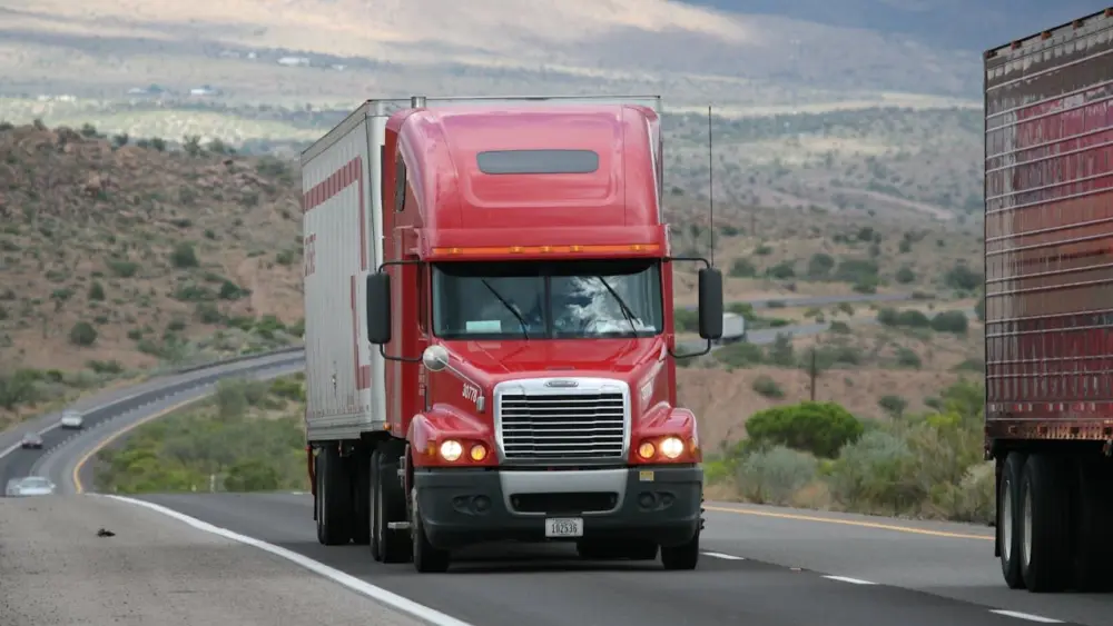 A red semi truck hauls a trailer along a highway through a desert landscape. Photo: CARLOSCRUZ ARTEGRAFIA / Pexels