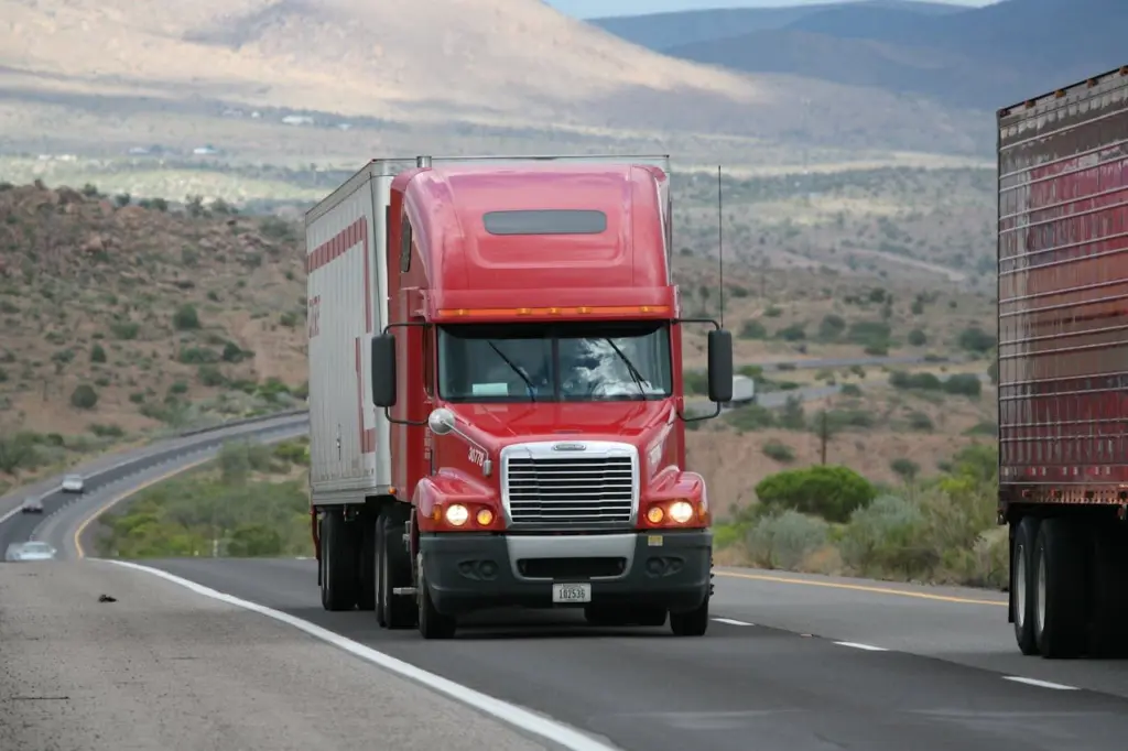 A red semi truck hauls a trailer along a highway through a desert landscape. Photo: CARLOSCRUZ ARTEGRAFIA / Pexels
