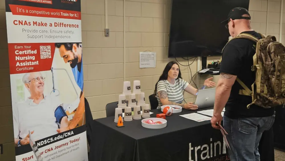 McKenna Melby of the North Dakota State College of Science speaks with a job fair attendee in Fargo, North Dakota, on July 28, 2026. Melby was recruiting potential students for the certified nursing assistant program.(Photo by Jeff Beach/North Dakota Monitor)