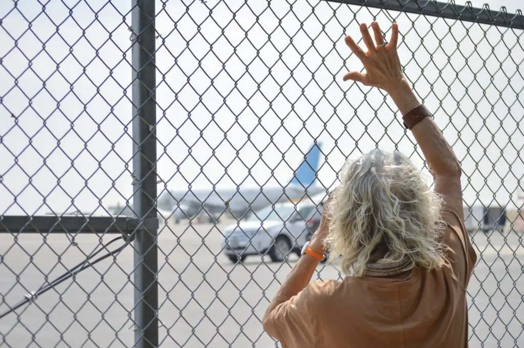 Maureen Newton waves as she uses binoculars to watch U.S. Immigration and Customs Enforcement detainees board a plane on Aug. 11, 2026, at the Magic Valley Regional Airport. (Photo by Laura Guido/Idaho Capital Sun)