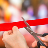 hand-with-scissors-cutting-red-ribbon-opening-ceremony-concept
