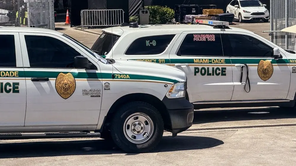 Two Miami-Dade police K-9 cars are parked near a metal security fence on a bright sunny day. Miami^ Florida^ USA^ June 16th 2025