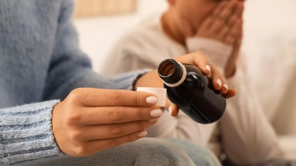 Mother giving cough syrup to her sick son in bed