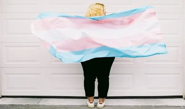 transgender-person-from-behind-wearing-pink-and-white-striped-sweatshirt-holds-transgender-flag