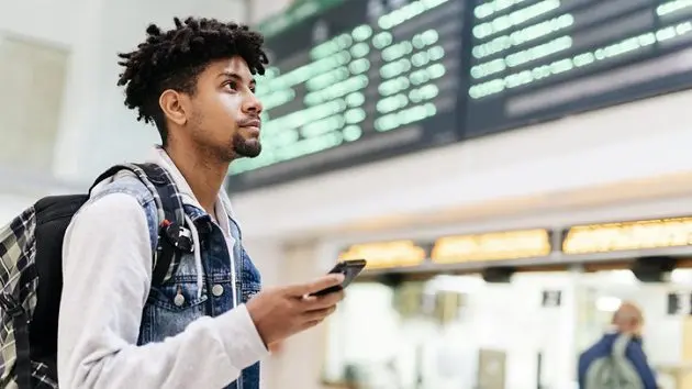 young-man-at-the-airport-looking-at-the-list-of-destinations-holding-a-cell-phone