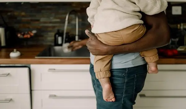 midsection-of-father-carrying-baby-boy-while-doing-chores-in-kitchen