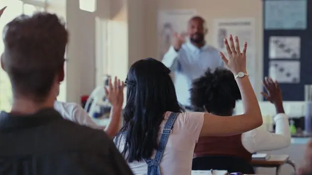 rearview-shot-of-students-raising-their-hands-during-a-lesson-with-a-teacher-in-a-classroom