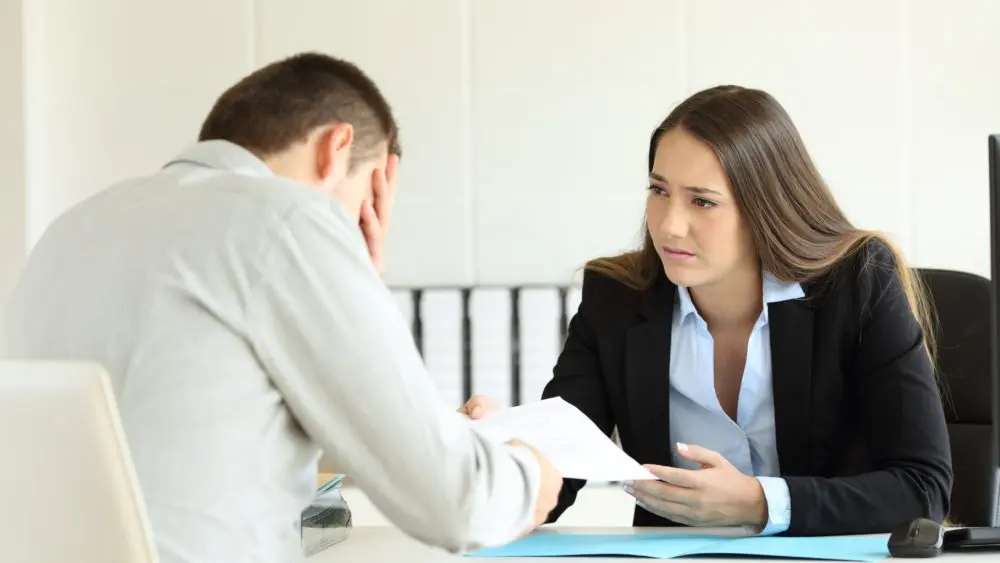 sadbossfiringanemployeesittinginherdesktopat
