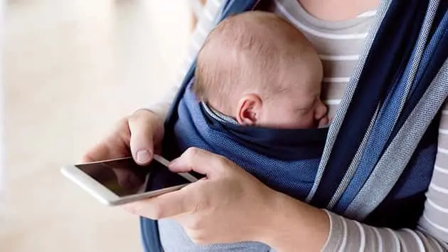 unrecognizable-mother-with-her-son-in-sling-holding-smartphone
