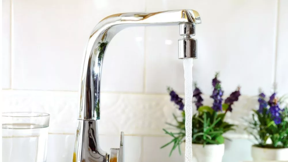 Open kitchen sink faucet flowing stream of water purified by domestic reverse osmosis with filters around. Front view. Horizontal composition.