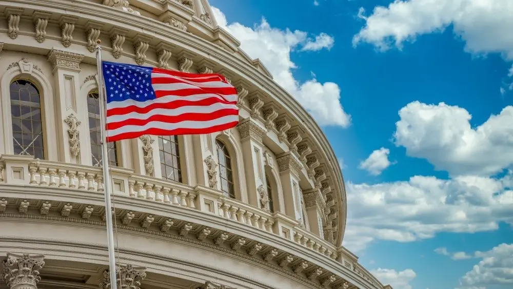The star spangled banner American flag flies proudly in front of the US capitol building in Washington DC with blue cloudy sky background