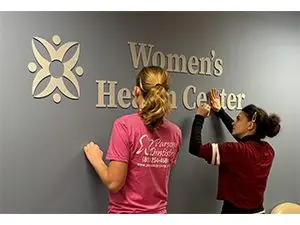 2femalestudentswithinstallingwomenshealthcentersign