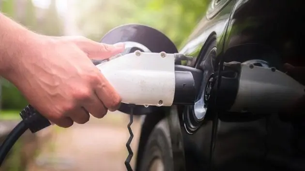 mans-hand-inserting-charger-plug-into-electric-car-in-green-environment-background-new-energy-vehicle-nev-is-being-loaded-with-electricity-power-ecology-modern-day-cars
