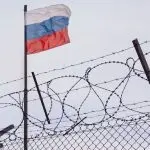View of russian flag behind barbed wire against cloudy sky. Concept anti-Russian sanctions. A border post on the border of Russia.