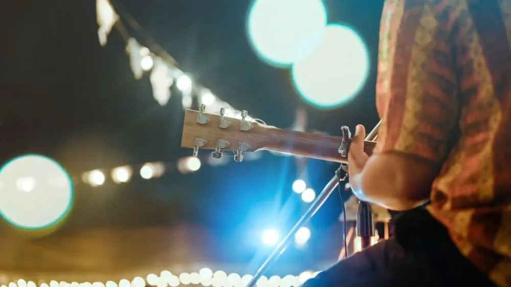 Musical and enjoyment concepts. Rear view of the man sitting play acoustic guitar on the outdoor concert with a microphone stand in the front.