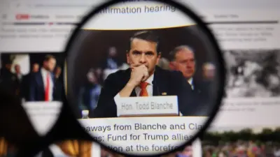 Close up through magnifying lens capturing legal professional Todd Blanche with nameplate at desk during hearing. Law and courtroom justice journalism concept.