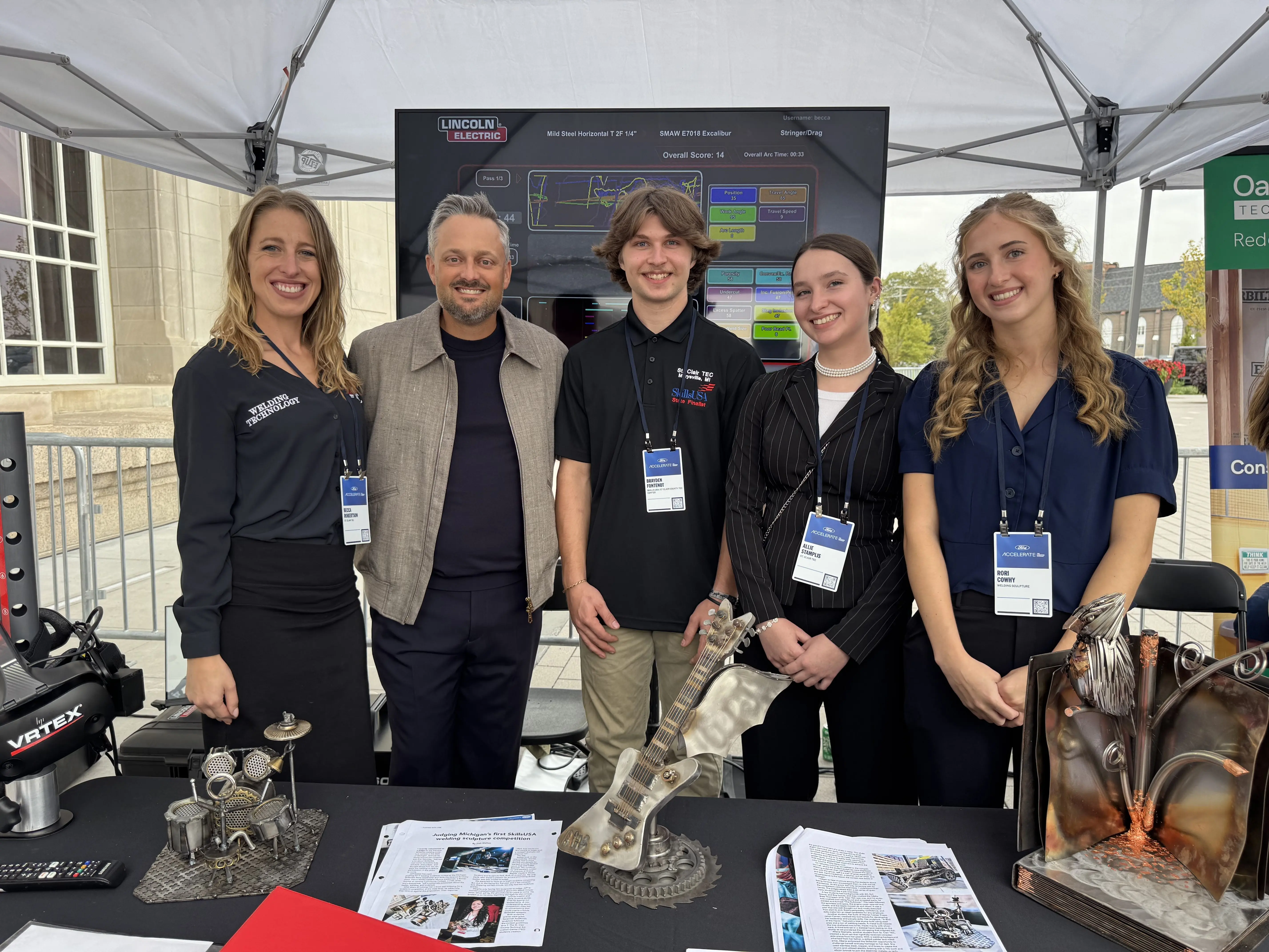 St. Clair County TEC Welding instructor Becca Robertson and Welding students Brayden Fontenot, Allie Stampliss, and Rori Cowhy pose with comedian and actor Nate Bargatze during Ford ACCELERATE Sept. 30 in Detroit.