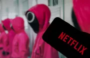 Netflix logo on the display of a smartphone in front of a television with the new series "Squid Game" ( focus on Netflix logo )