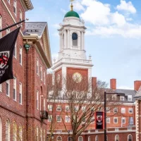 View of the architecture of the famous Harvard University in Cambridge^ Massachusetts^ USA showcasing it brick buildings with some students and locals passing by . Cambridge^ MA^ USA - March 15^ 2024