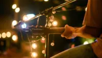 Rear view of the man sitting play acoustic guitar on the outdoor concert with a microphone stand in the front^ musical concept.