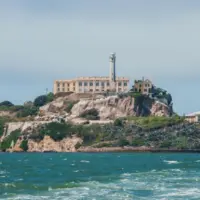 Alcatraz Island in San Francisco Bay^ California^ USA^ viewed from the water. Shows rugged terrain^ prison building^ lighthouse^ and choppy water under clear sky.