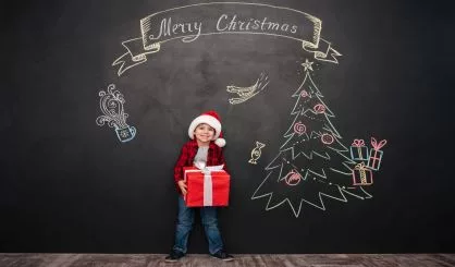 cute-child-holding-big-gift-near-christmas-drawing-on-blackboard