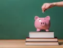 person-depositing-money-in-a-piggy-bank-on-top-of-books-with-chalkboard