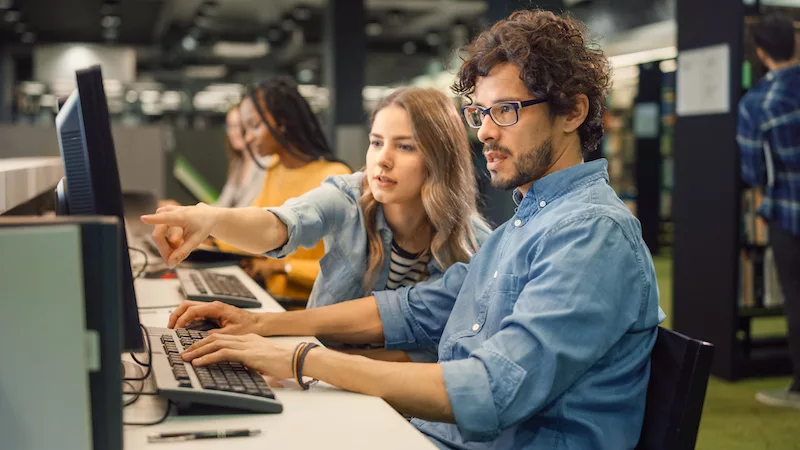 university-library-bright-caucasian-girl-and-smart-boy-together-work-on-computers-chat-discuss-class-assignment-explain-and-advice-each-other-diverse-group-of-students-exam-study-teamwork