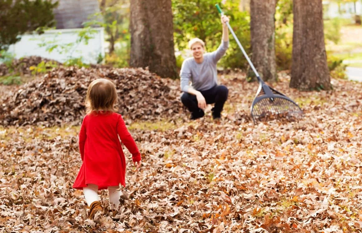 toddler-girl-running-to-her-father-raking-leaves-in-the-fall