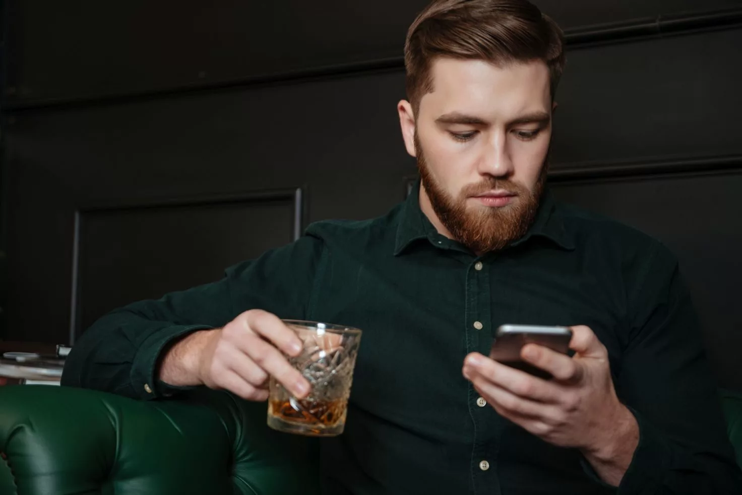 serious-man-sitting-and-drinking-whiskey-while-holding-cellphone