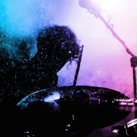 Silhouette of a drummer playing under vibrant pink and blue stage lights^ capturing the energy and motion of a live music performance.