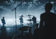 rock band viewed from behind the stage performing to sold-out audience; view of drummers^ guitarists in silhouette in hazy photo