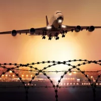 Passenger plane takes off at dusk^ in the background the lights of the airport can be seen and in the foreground a barbed wire fence
