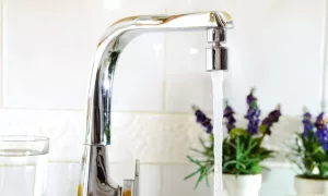 Open kitchen sink faucet flowing stream of water purified by domestic reverse osmosis with filters around. Front view. Horizontal composition.