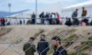 Barbed wire in refugee camp. Migrants behind chain link fence in camp. Group of people behind fence. Concept of prison^ freedom^ barrier^ security and migration. Refugees on their way to EU.