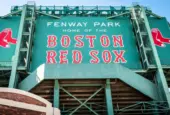 View of the historic architecture of the Fenway Park Stadium showcasing its signs^ brick walls^ statues^ and the famous green color and red letters of the red sox. Boston^ MA^ USA - March 10^ 2023