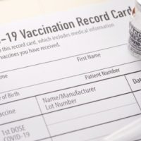 covid19-vaccination-record-card-with-vials-and-syringe-picture-id1289454645