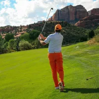 Golfer mid-swing on a beautiful golf course with mountains in the distance.