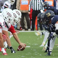 Two football teams lined up, white and black uniforms, red team with ball at the center, about to hike.