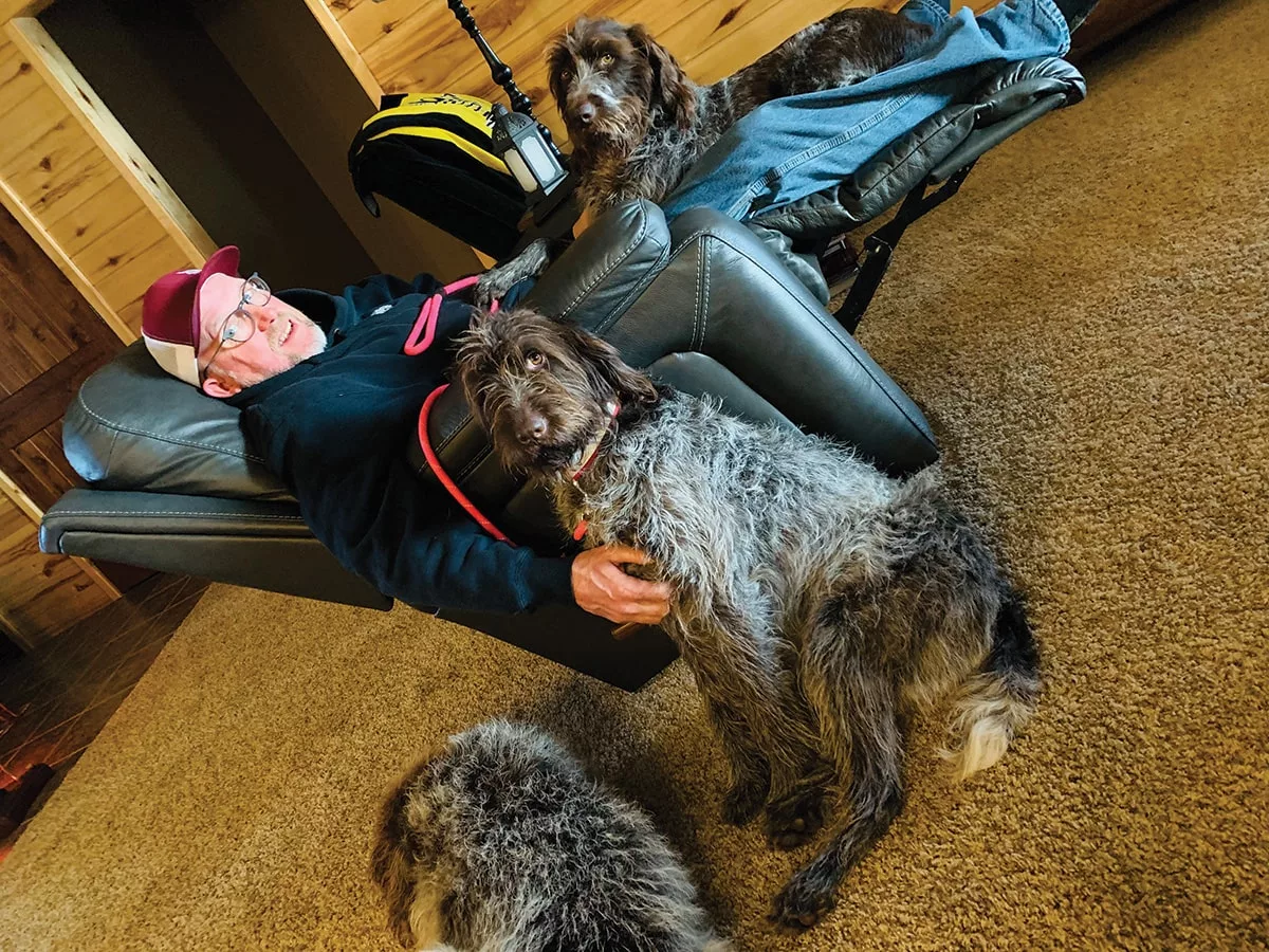 Jimmy Clark seated in a recliner in his home, surrounded by his three dogs.