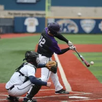 Batter swinging at baseball while catcher observes on baseball field.