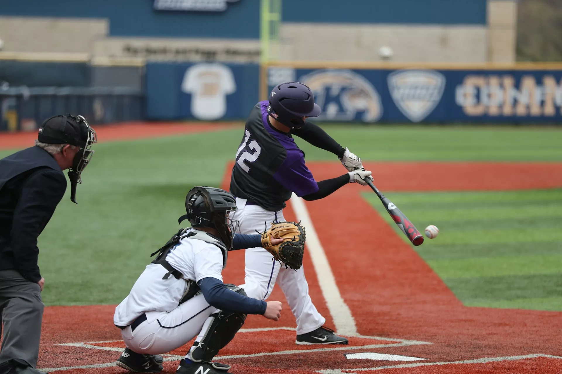Batter swinging at baseball while catcher observes on baseball field.