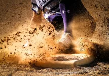 Softball player sliding into home plate, creating a cloud of dirt.