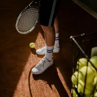 Boy holding tennis racket next to basket of tennis balls