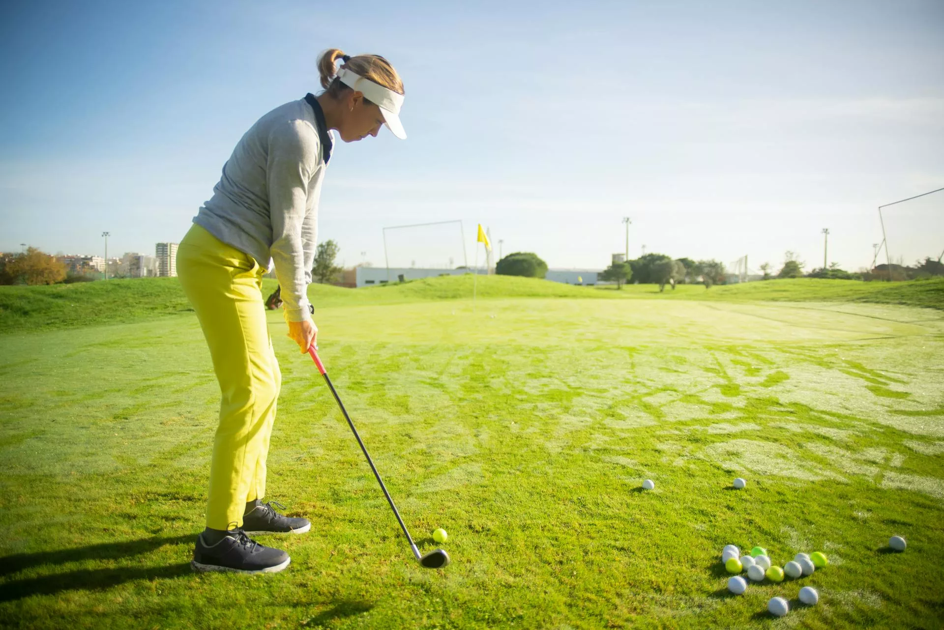 Woman in yellow pants hitting golf balls on the driving range.