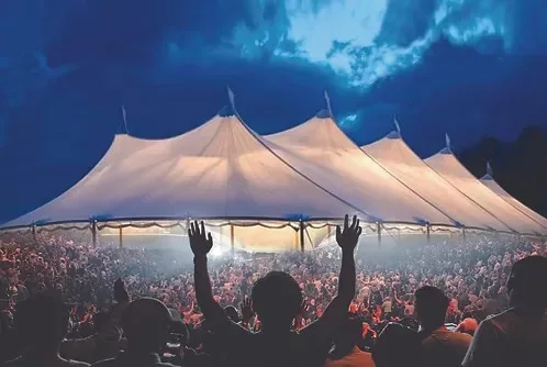 A group of people standing outside a tent, worshiping under the night sky.