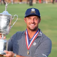 Bryson DeChambeau holding up the US Open trophy with a joyful expression, celebrating his victory.