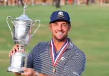 Bryson DeChambeau holding up the US Open trophy with a joyful expression, celebrating his victory.