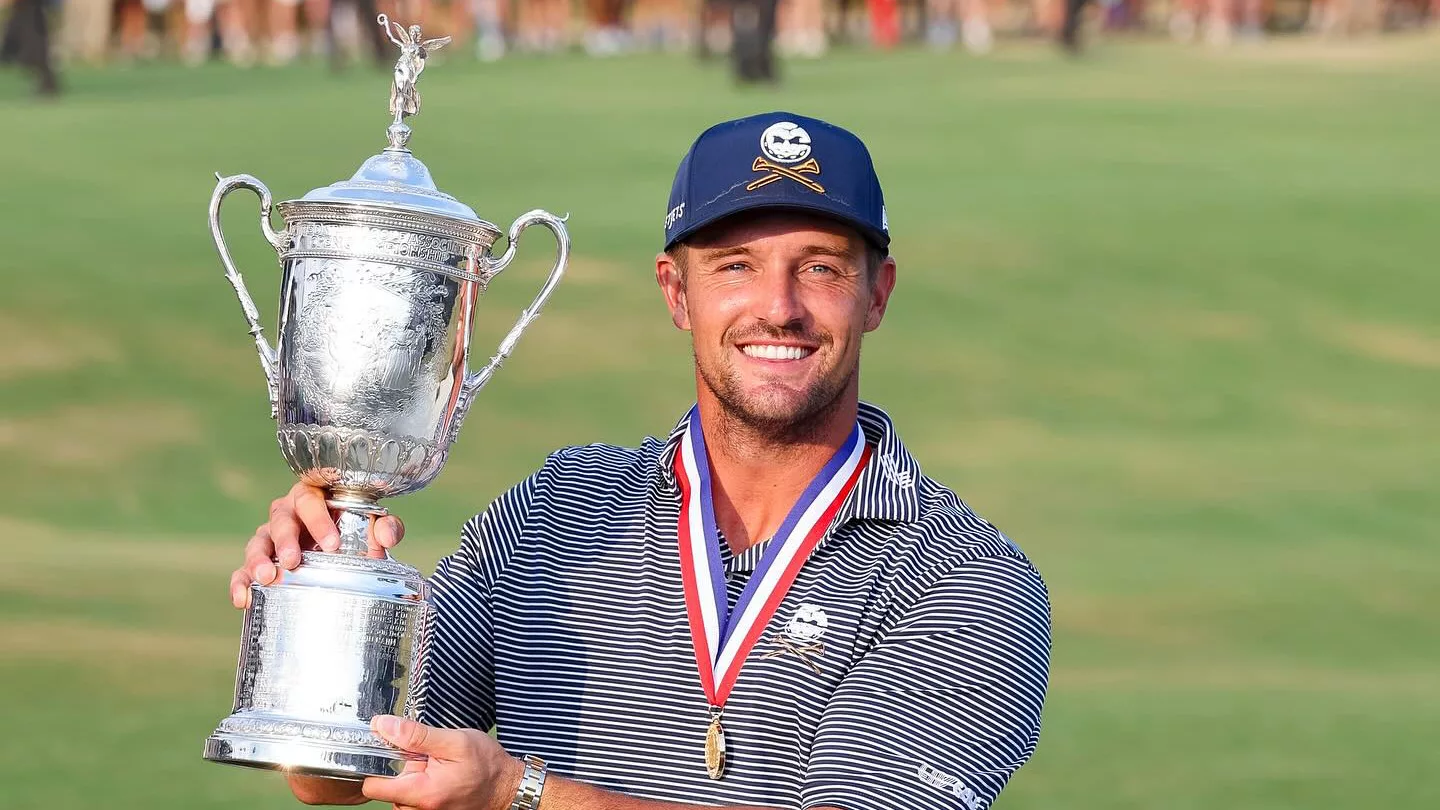 Bryson DeChambeau holding up the US Open trophy with a joyful expression, celebrating his victory.